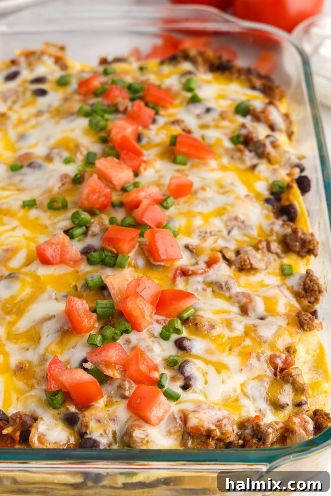 Close up view of the bubbling, cheesy top of Mexican Lasagna in a pan, beautifully golden and garnished with fresh herbs