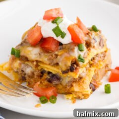 A perfectly sliced piece of Mexican Lasagna on a white plate, garnished with fresh cilantro and a dollop of sour cream