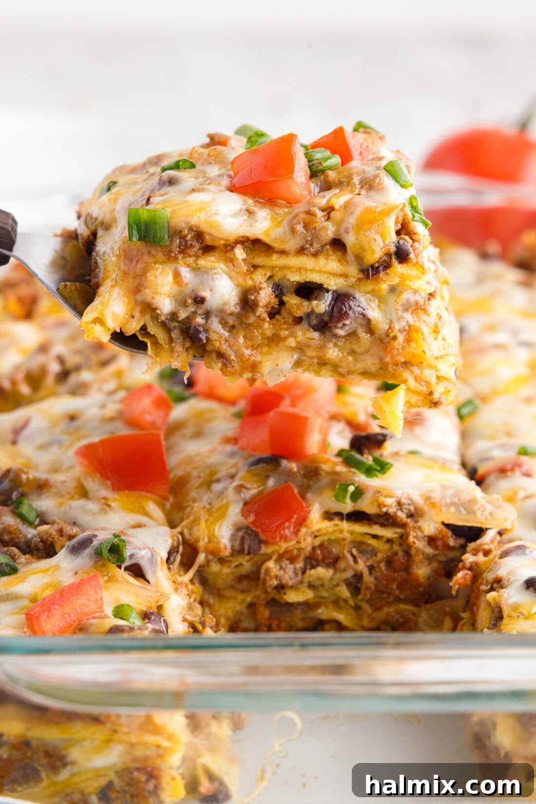 A generous serving of Mexican Lasagna being lifted from the pan with a spatula, showing gooey melted cheese and distinct layers