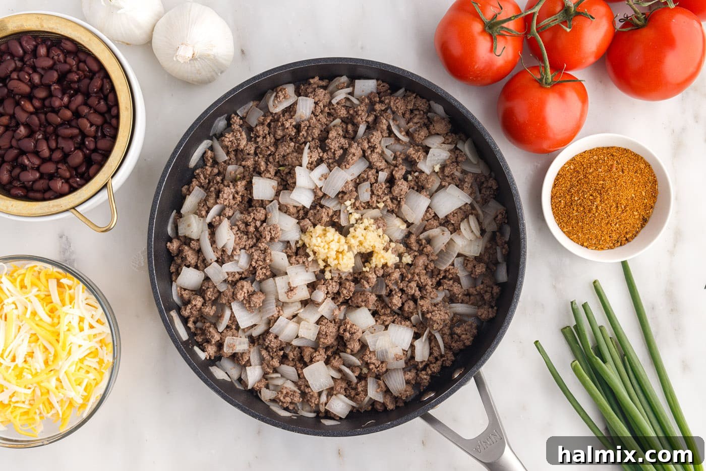 Adding minced garlic to the browned ground beef and onion mixture in a skillet, filling the air with aroma
