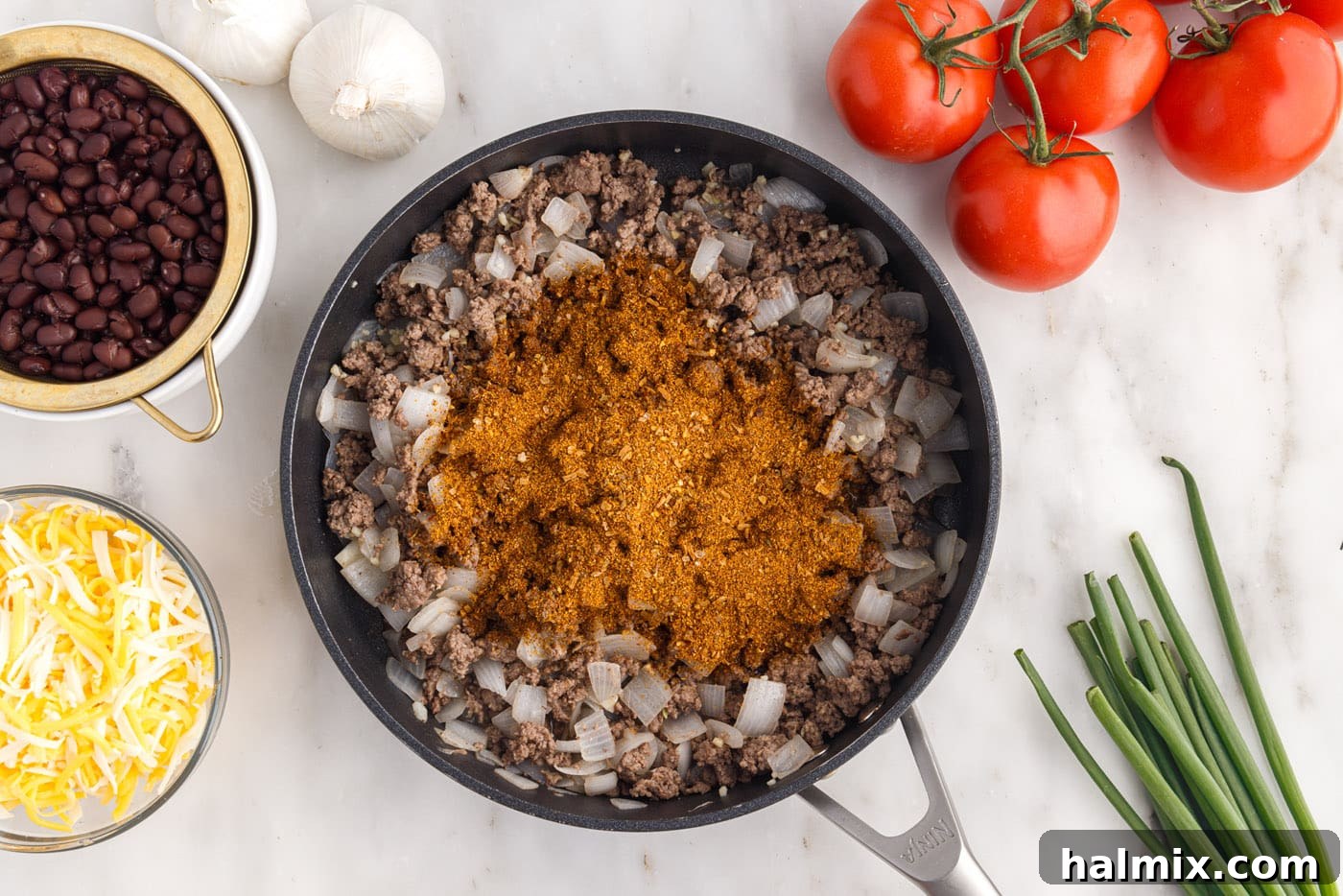 Taco seasoning being stirred into the ground beef and onion mixture in a skillet, creating a rich sauce