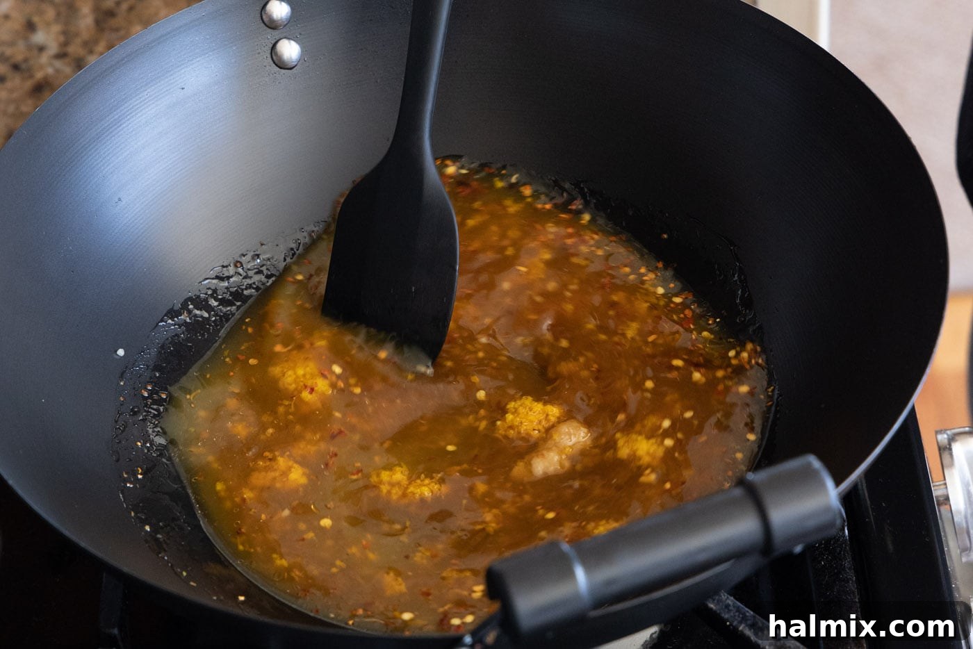 spatula stirring orange chicken sauce ingredients in a skillet