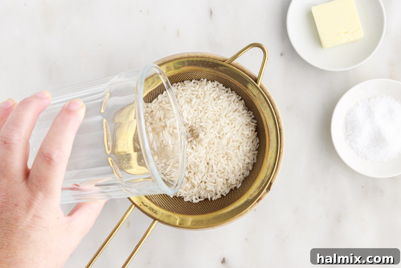 Pouring water over white rice in a sieve to rinse it