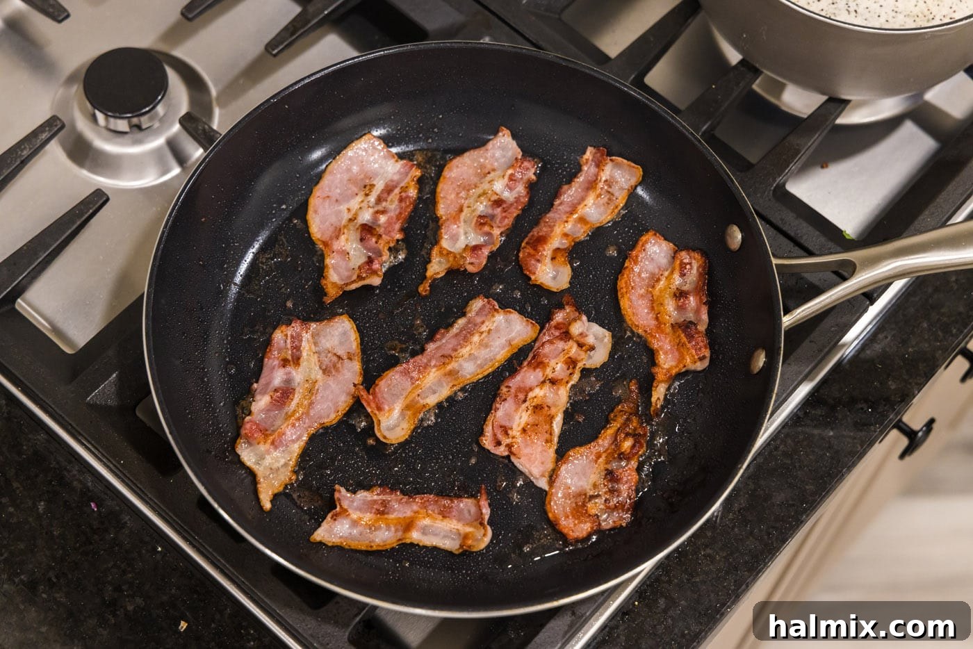 Bacon strips sizzling and cooking to a perfect crisp in a hot skillet, releasing their flavorful grease.
