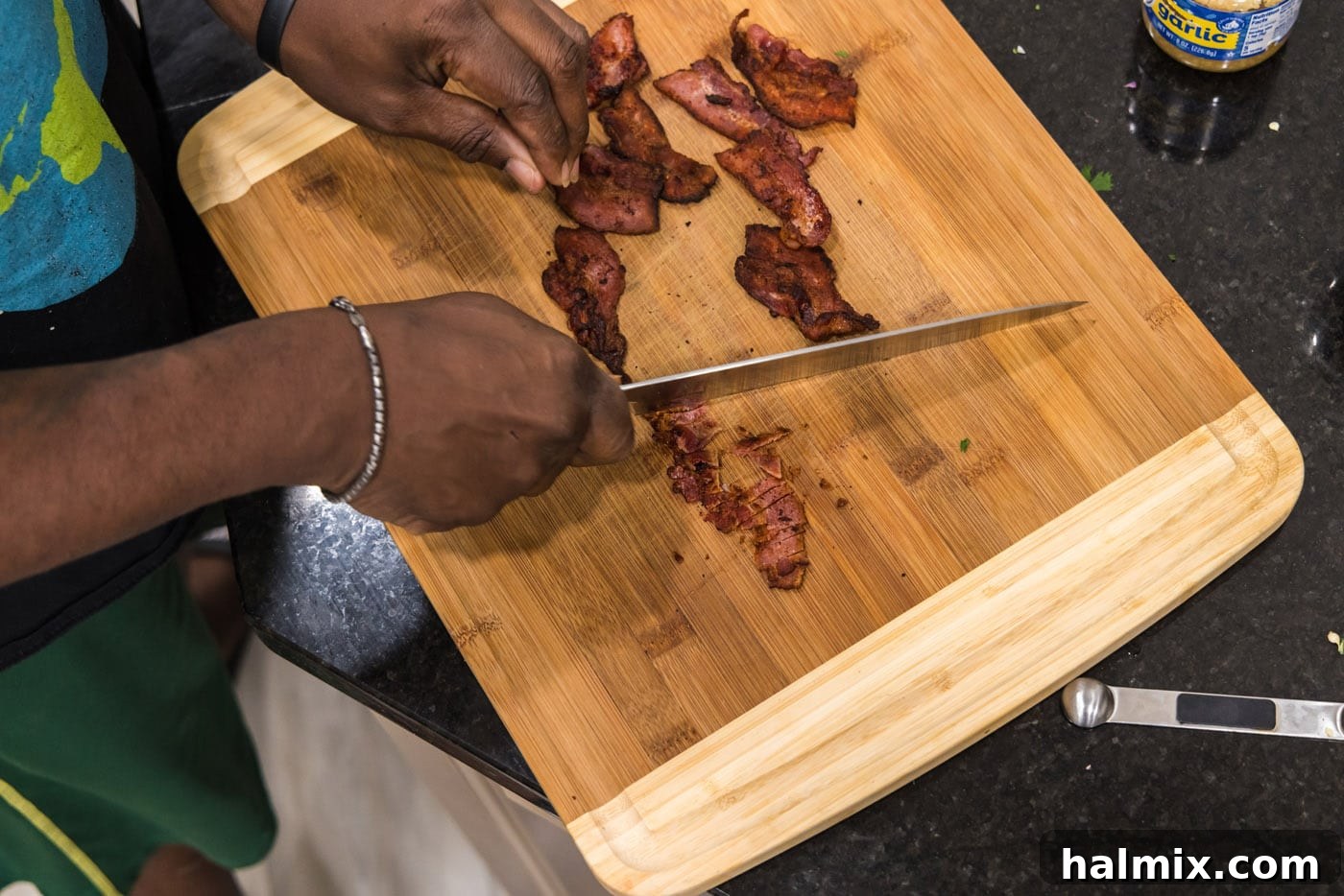 Crispy bacon being chopped on a cutting board into small, even pieces for garnish.