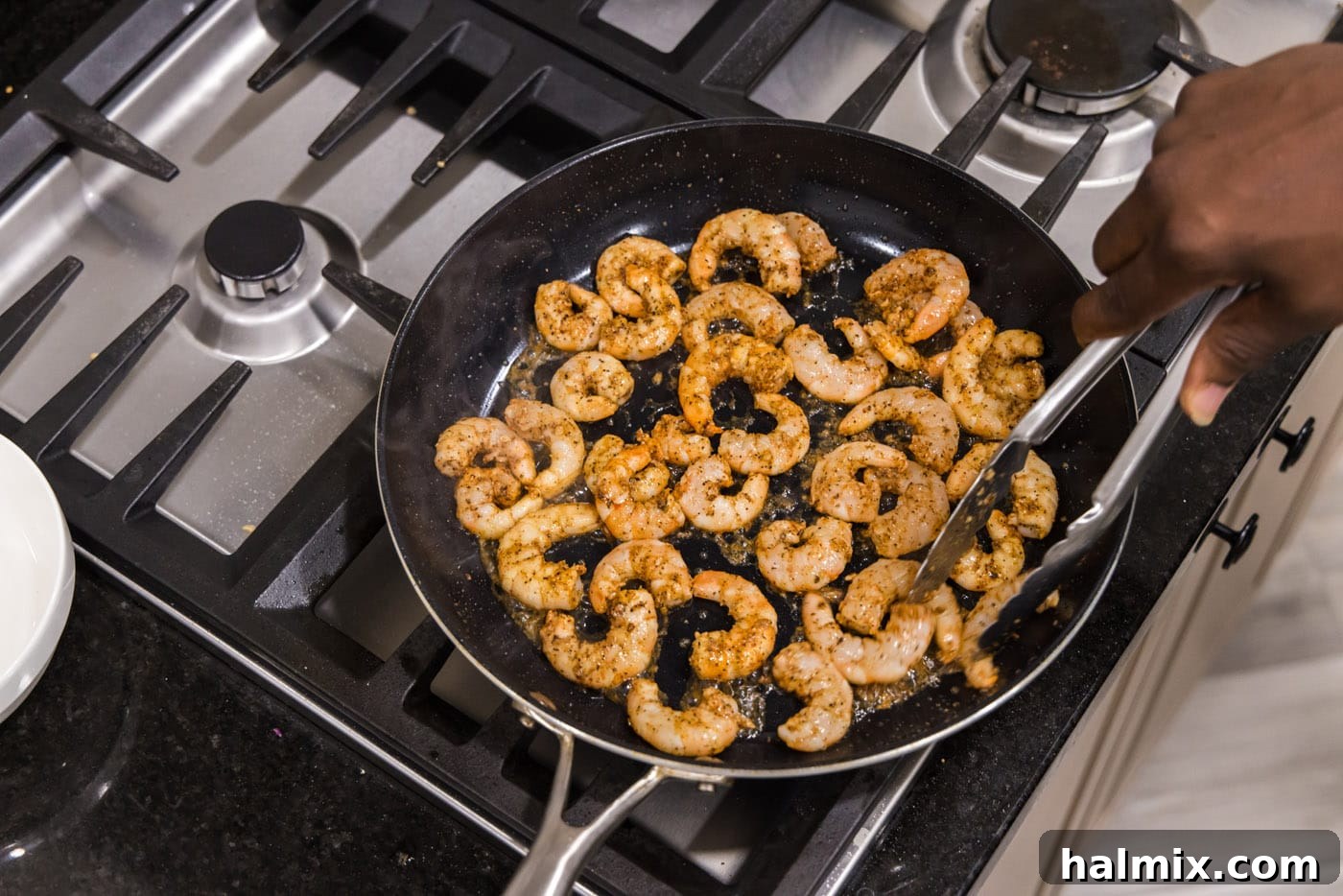 Cajun seasoned shrimp and minced garlic cooking in flavorful bacon grease in a skillet, turning pink and opaque.