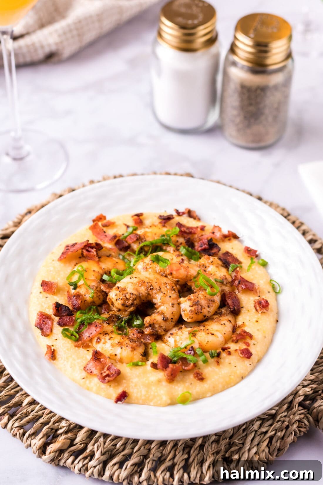 A perfectly plated bowl of Cheesy Shrimp and Grits, garnished with crispy bacon and fresh green onions, ready to be enjoyed.