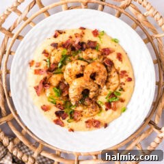 Overhead photo of a plate of Shrimp and Grits, showcasing the complete dish ready to eat, with crispy bacon and green onion garnish.