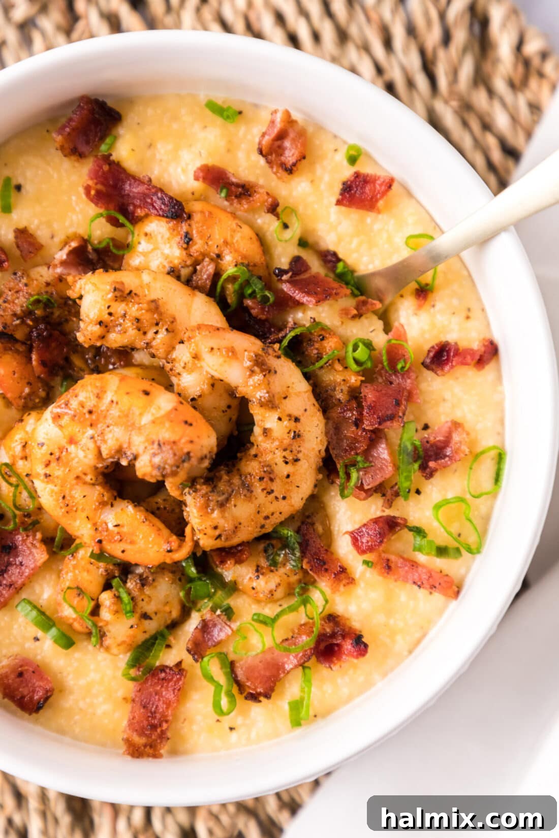 A vibrant bowl of Cheesy Shrimp and Grits, showcasing the golden shrimp, crispy bacon, and creamy texture, garnished with green onions.