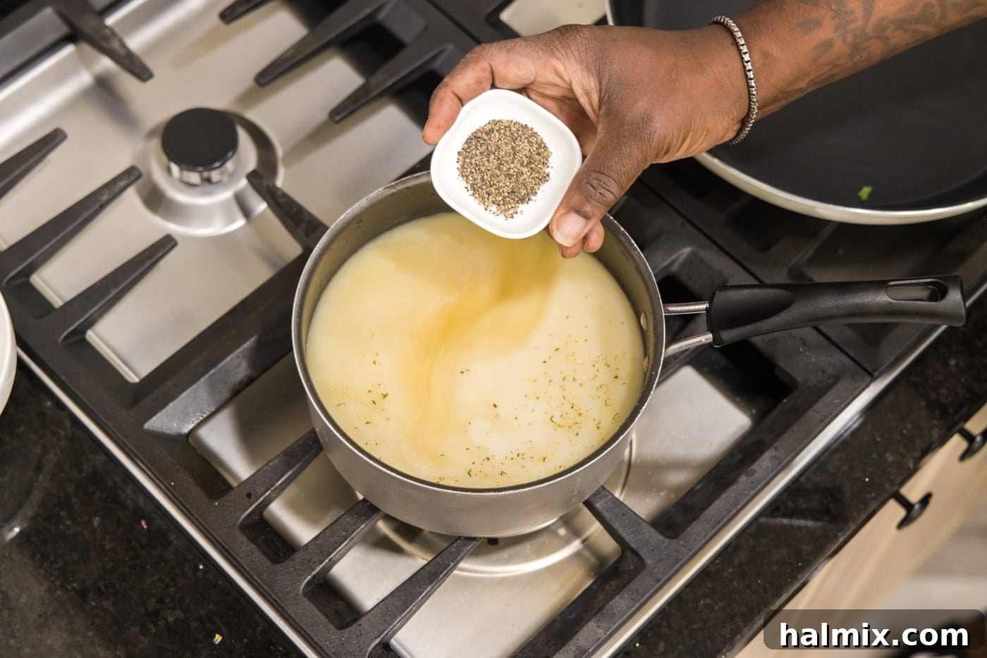 Chicken broth, milk, garlic salt, and pepper simmering in a saucepan, creating the flavorful base for creamy grits.