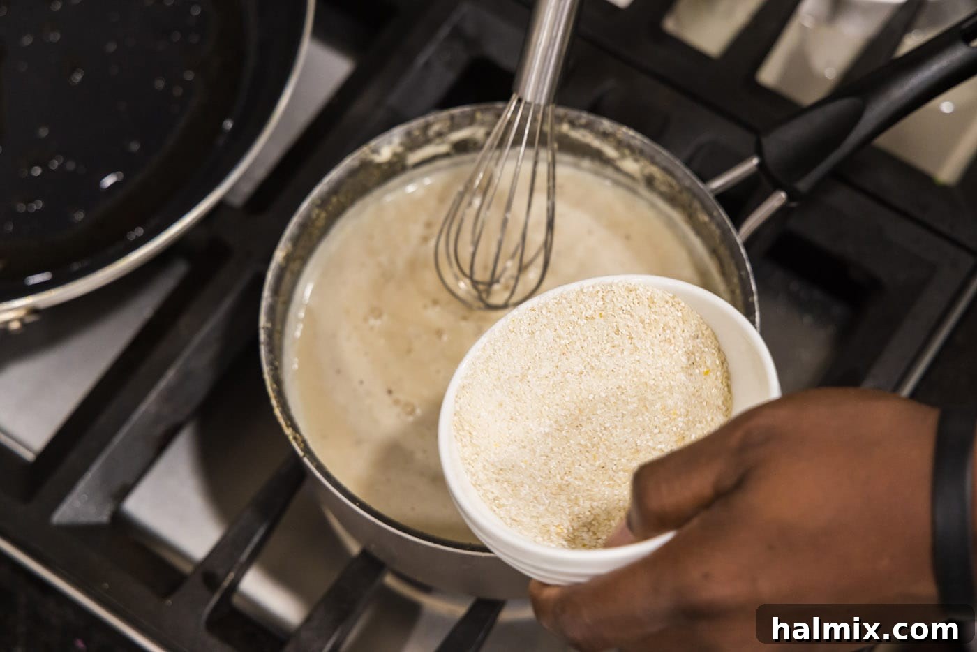 Whisking grits into the simmering liquid in a saucepan to prevent lumps and ensure a smooth texture.