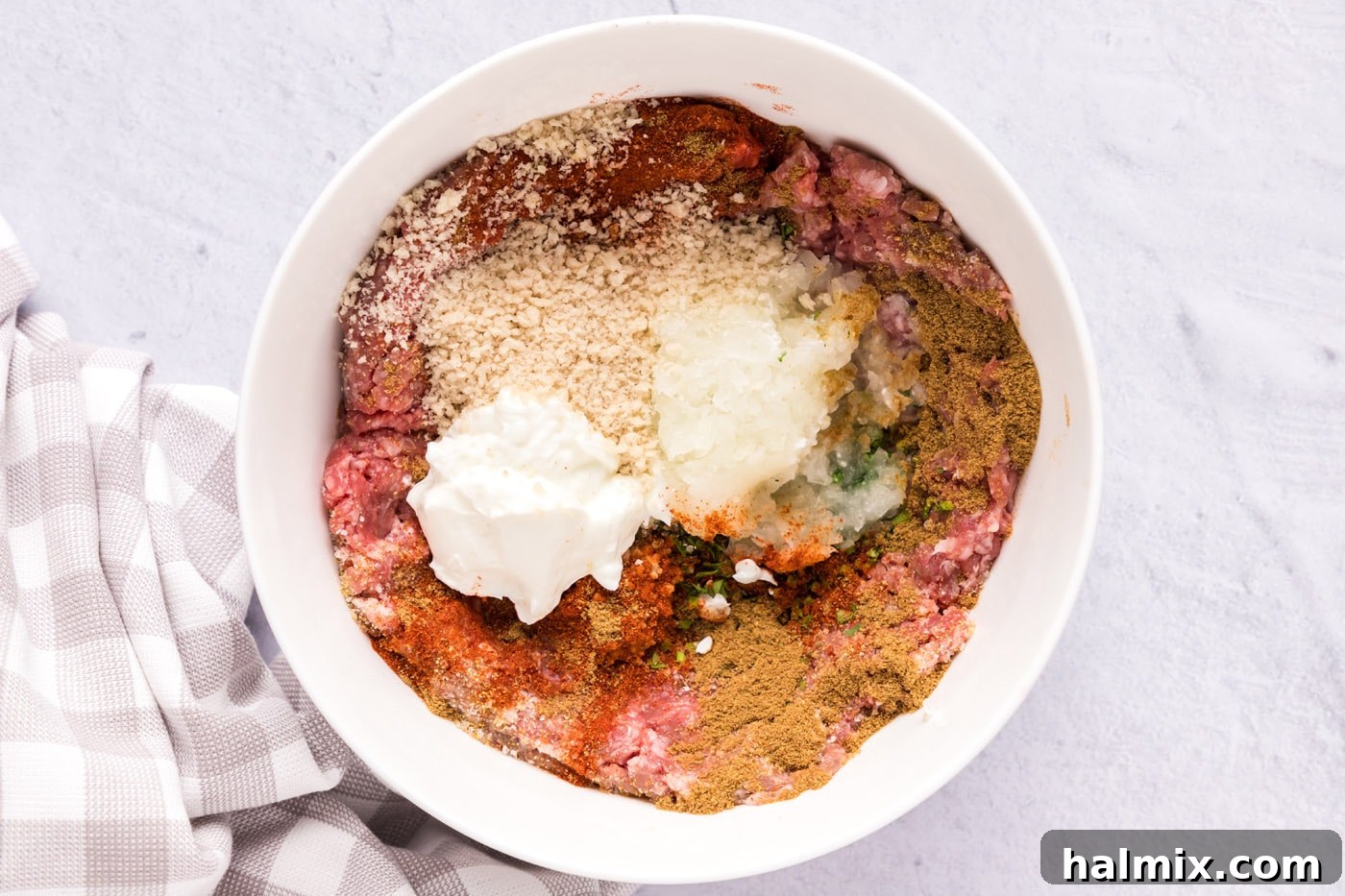 Ground lamb, breadcrumbs, seasonings, grated onion, and Greek yogurt thoroughly combined in a bowl, ready to be formed into meatballs.