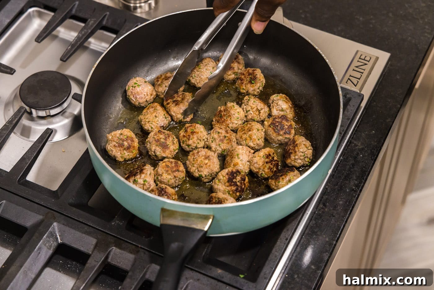 Lamb meatballs being turned and browned in a hot skillet, showcasing their developing crispy exterior.