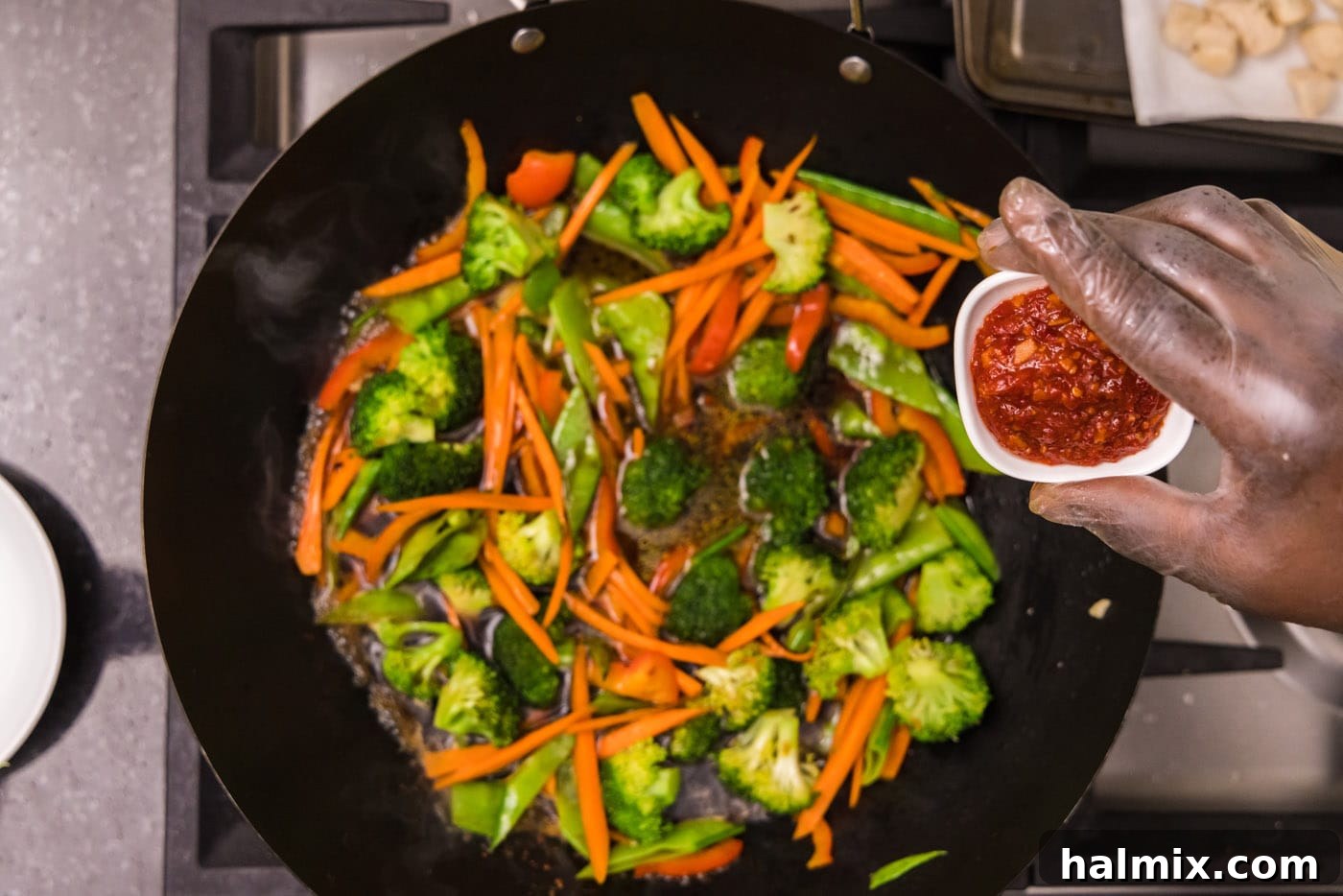 Asian chili garlic sauce over wok with vegetables