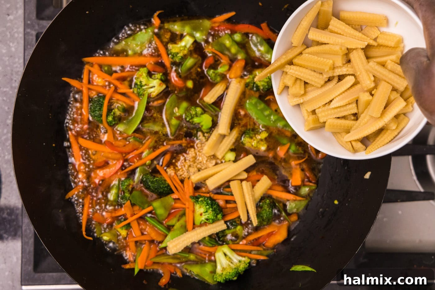 adding sliced baby corn to wok with vegetables