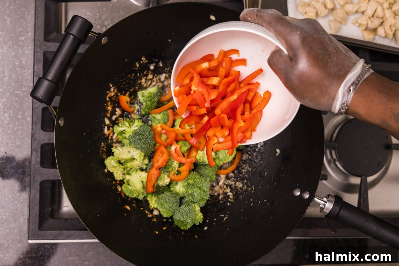 adding sliced red bell pepper to wok with broccoli