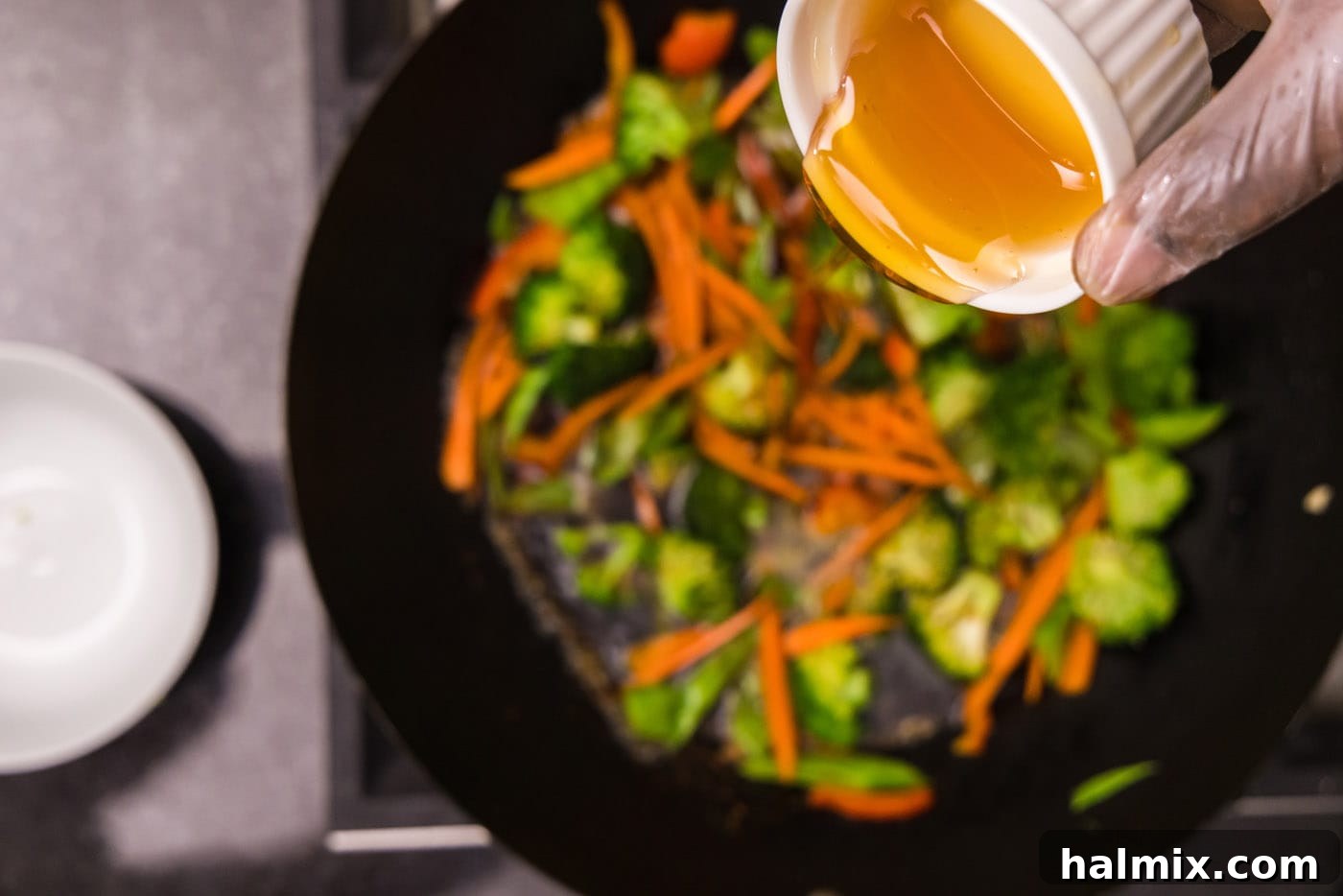 pouring honey into wok with vegetables