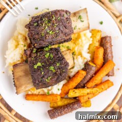 Overhead photo of two Beef Short Ribs over mashed potatoes, garnished with herbs.