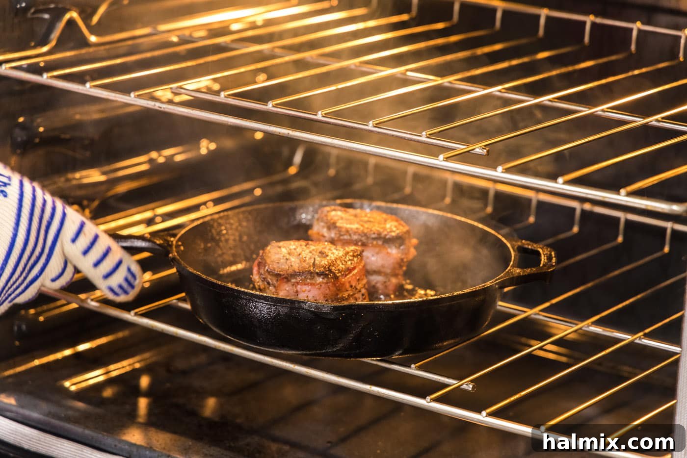 Bacon wrapped filet mignon steaks baking in an oven-proof skillet within the hot oven, completing the cooking process.