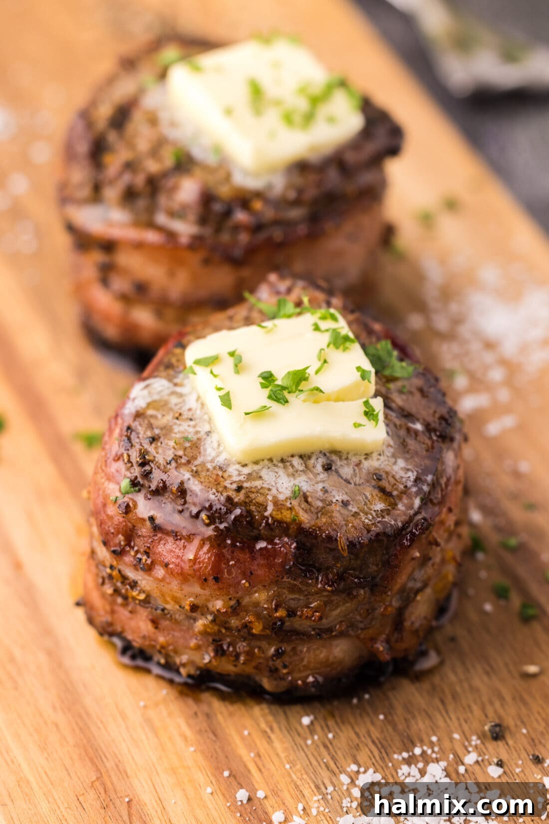 Two perfectly seared and bacon-wrapped filet mignon steaks resting on a serving platter, showcasing their enticing crust and ready for slicing.