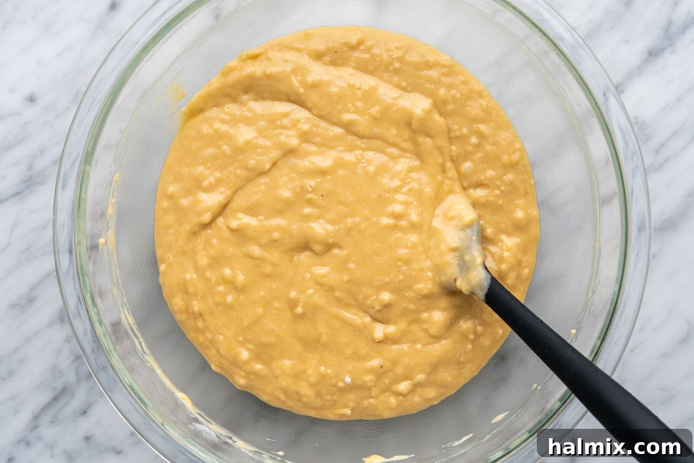 Muffin batter in a bowl with a rubber spatula, showing its slightly lumpy texture