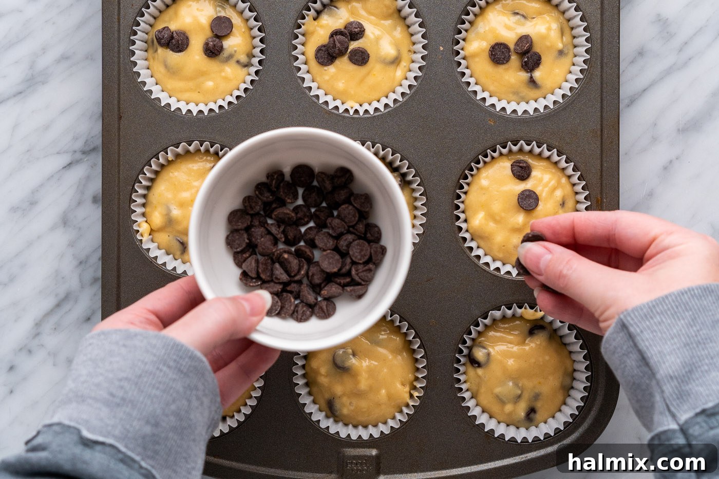 Adding extra chocolate chips on top of muffin batter in a pan for an extra burst of flavor