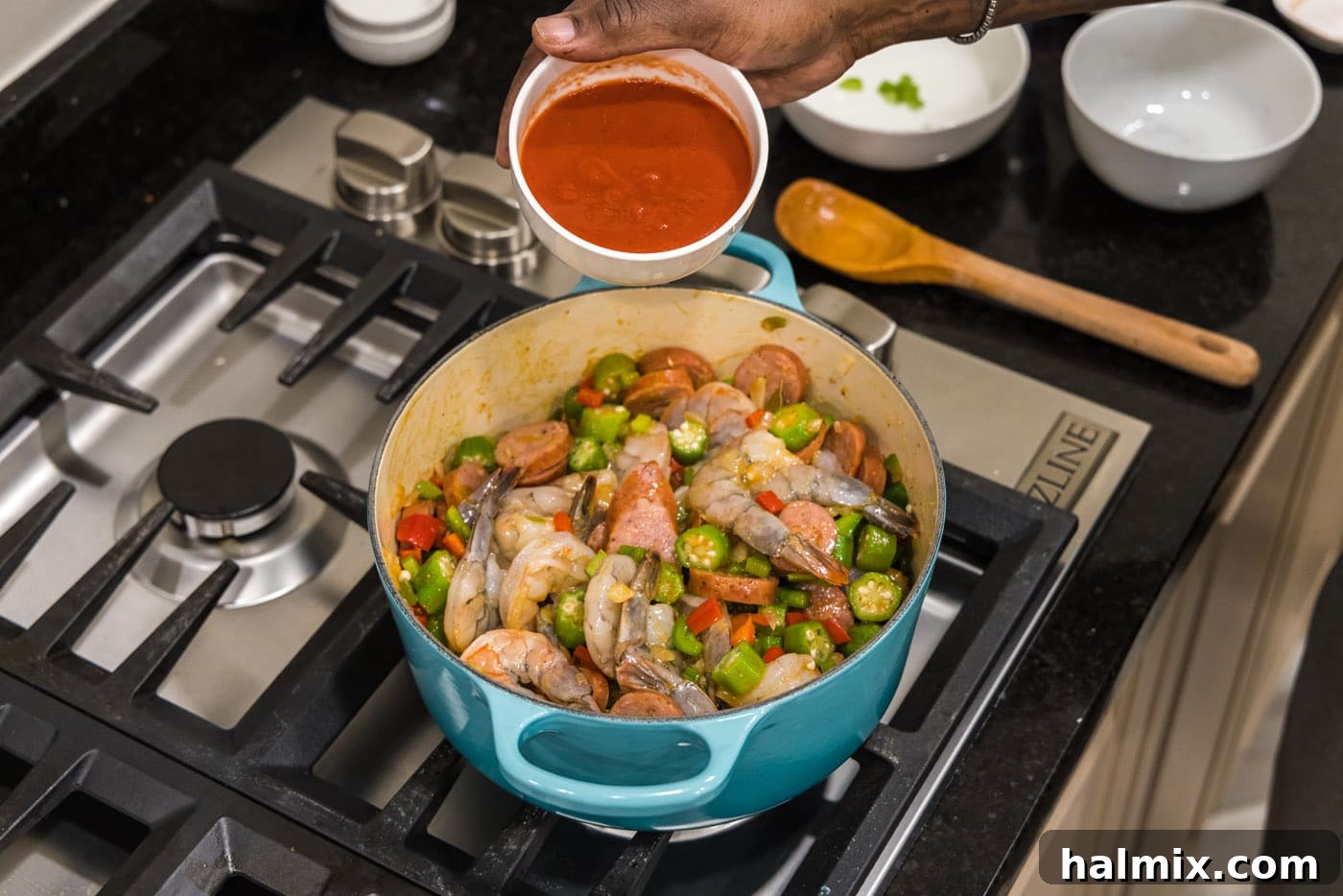 Bayou Blend 12 Tomato sauce being added over the simmering pot of shrimp, sausage, and vegetables, adding color and tang.
