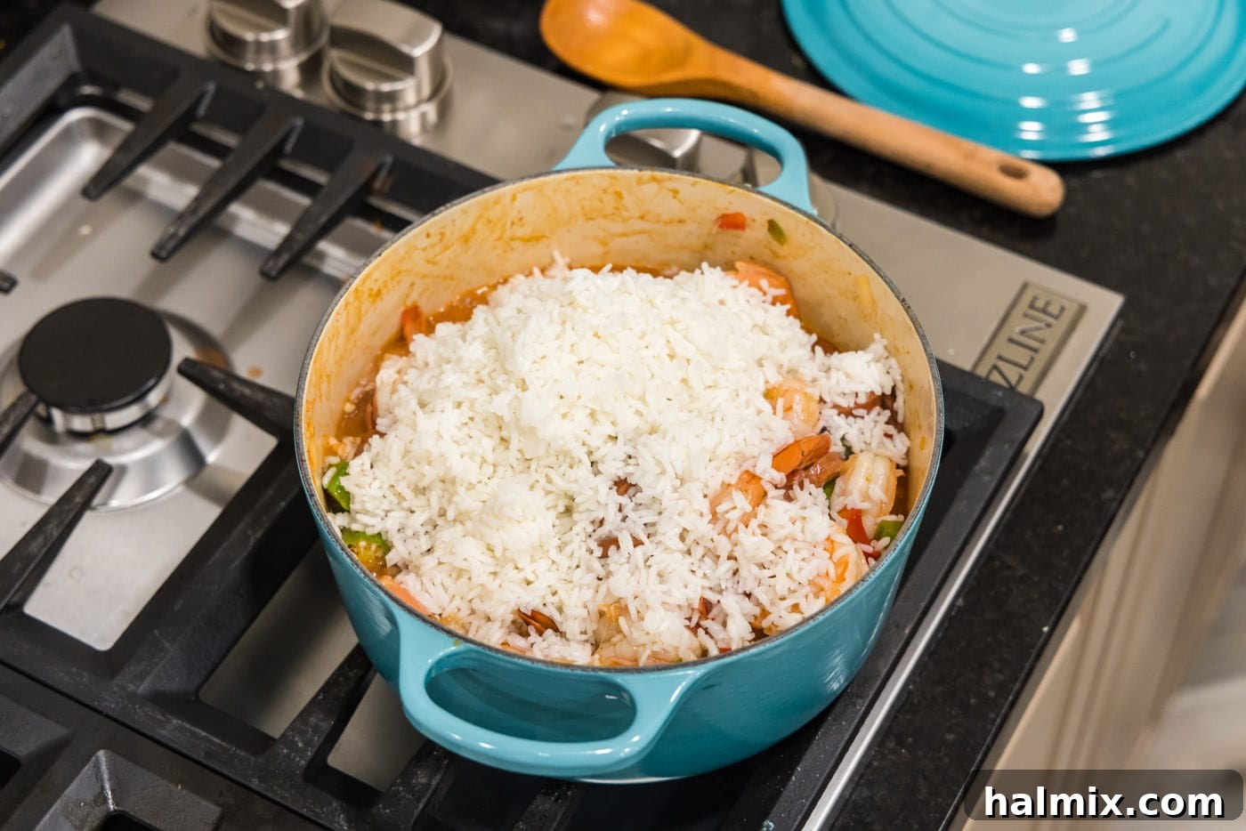 Bayou Blend 13 Cooked white rice spooned on top of the jambalaya mixture in a Dutch oven, ready to be combined.