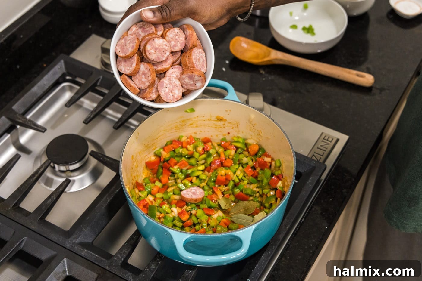 Bayou Blend 8 Sliced smoked sausage being added to the pot with the bell peppers, onion, and celery, preparing for a flavorful simmer.