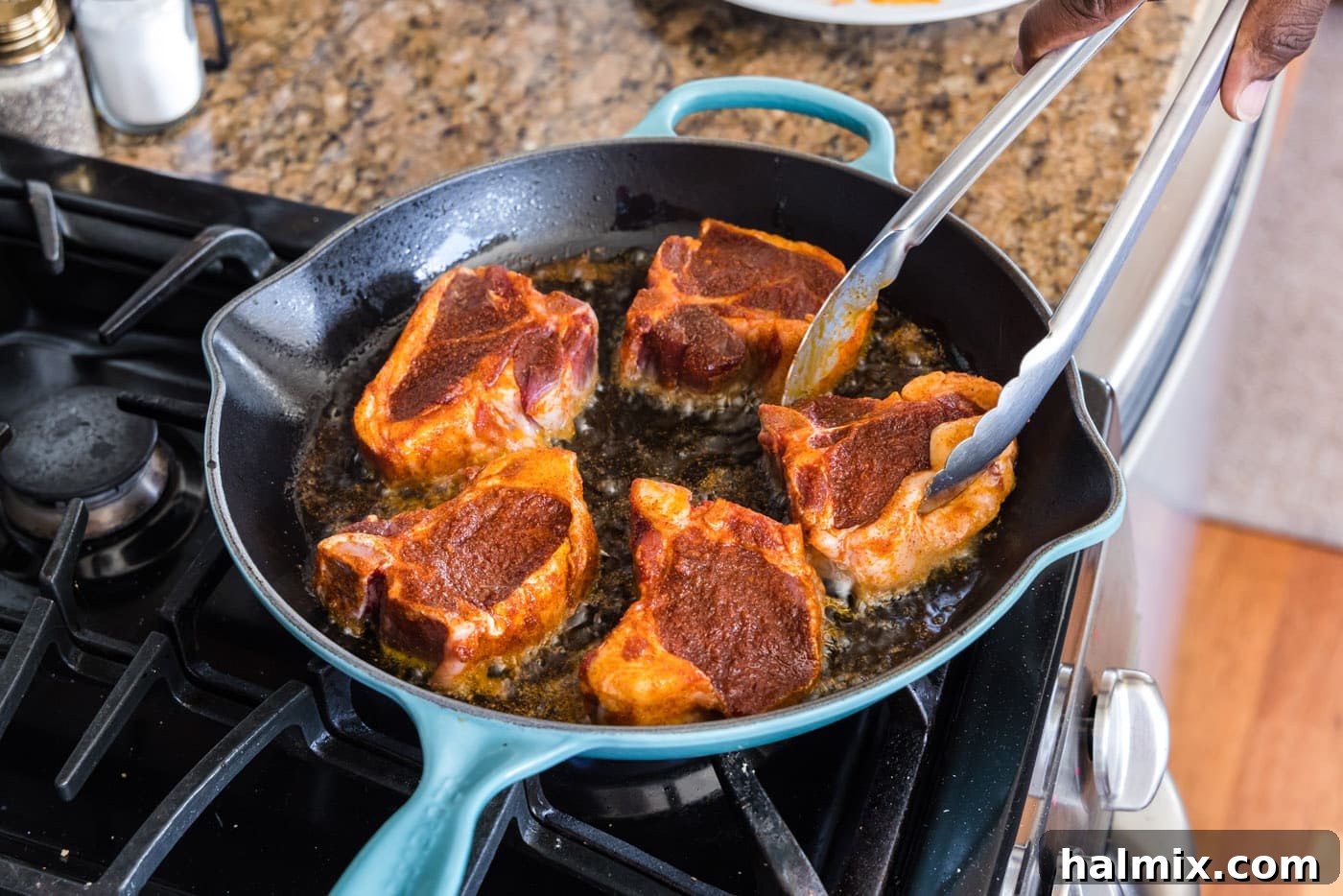 Using tongs to flip lamb loin chops in a skillet