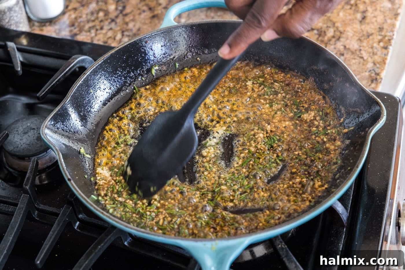 Spatula mixing minced garlic, fresh rosemary, melted butter, and oil in a skillet to create a fragrant sauce