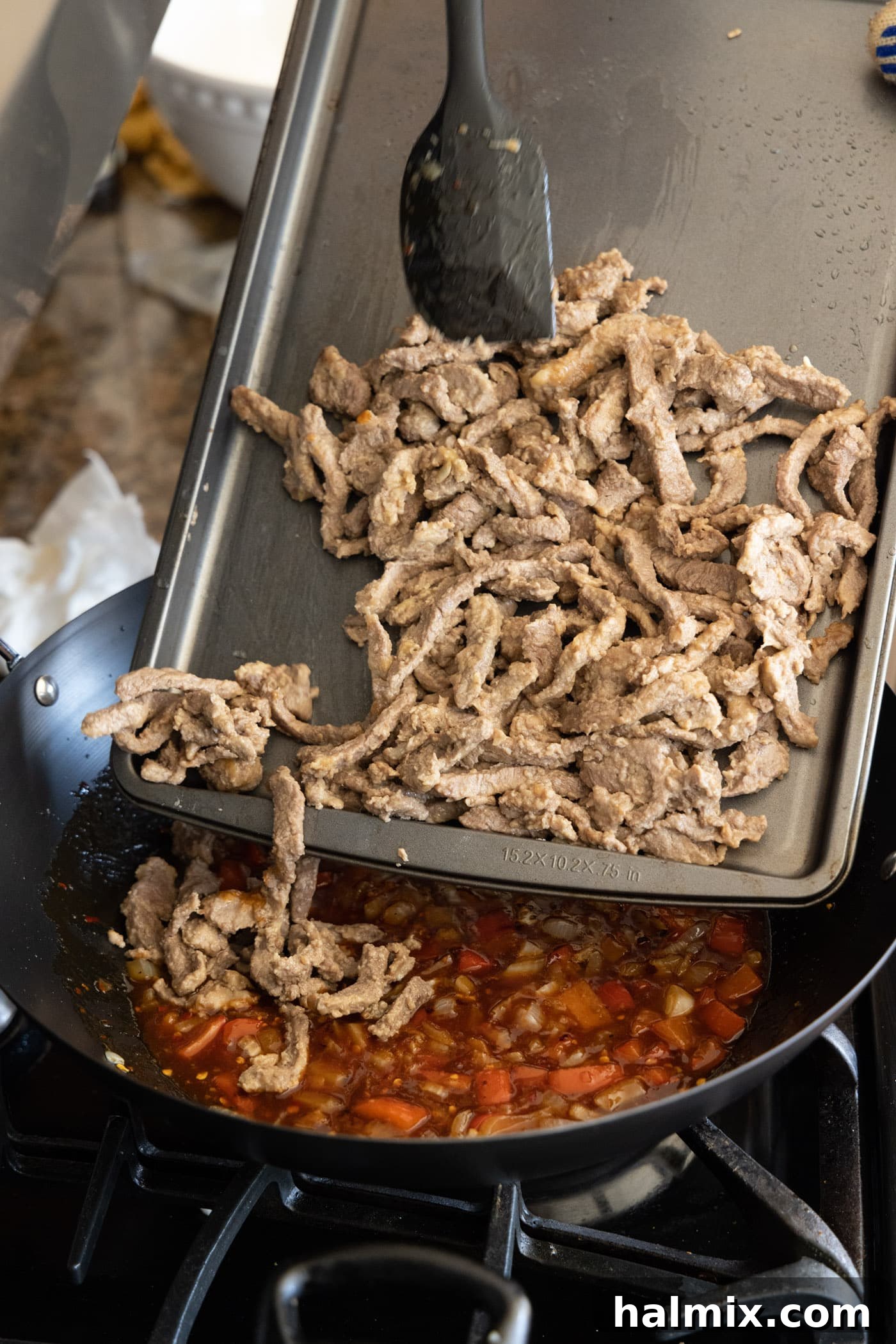 adding cooked beef to skillet with sauce and vegetables