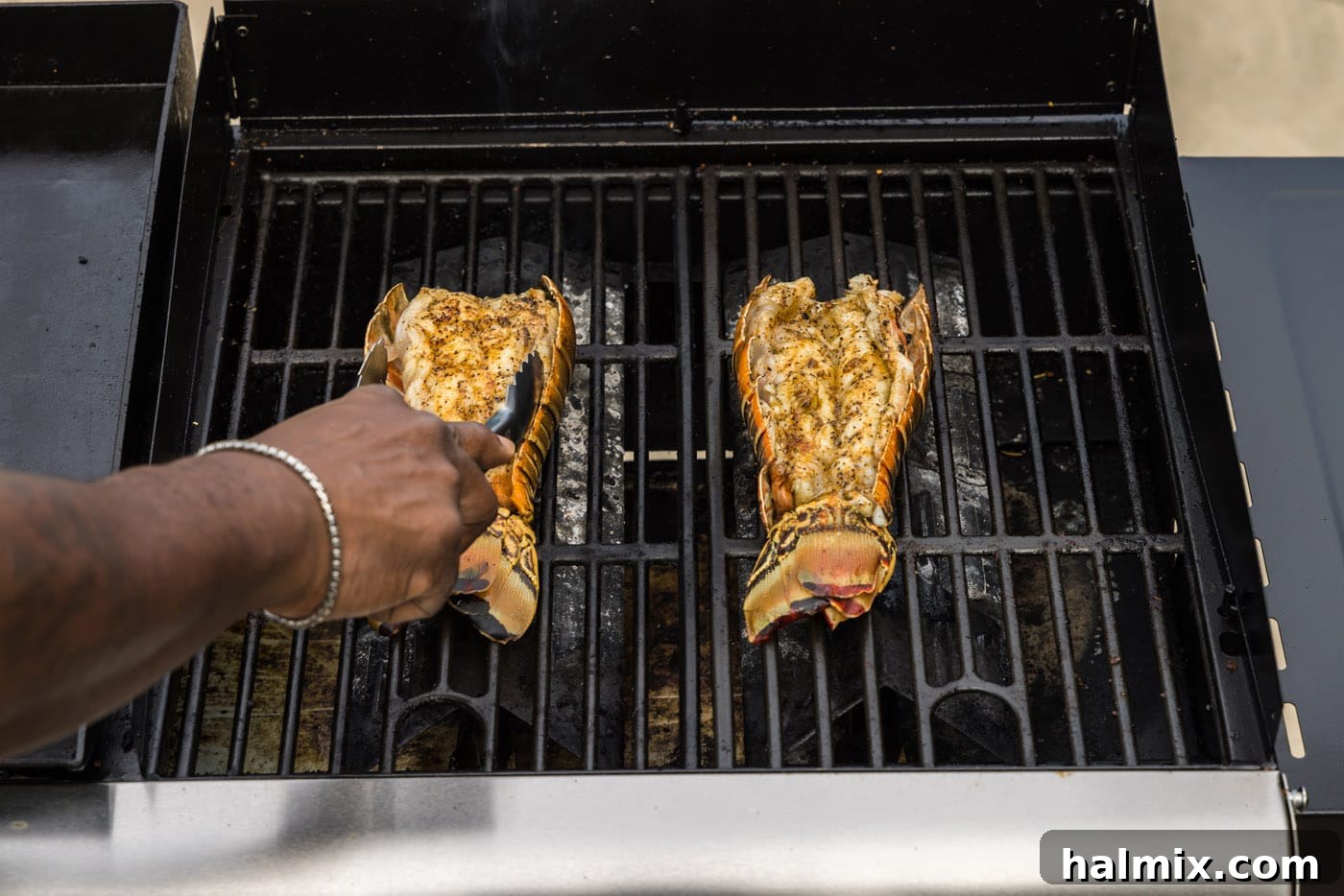 Tongs carefully flipping lobster tails on the grill, ensuring even cooking.