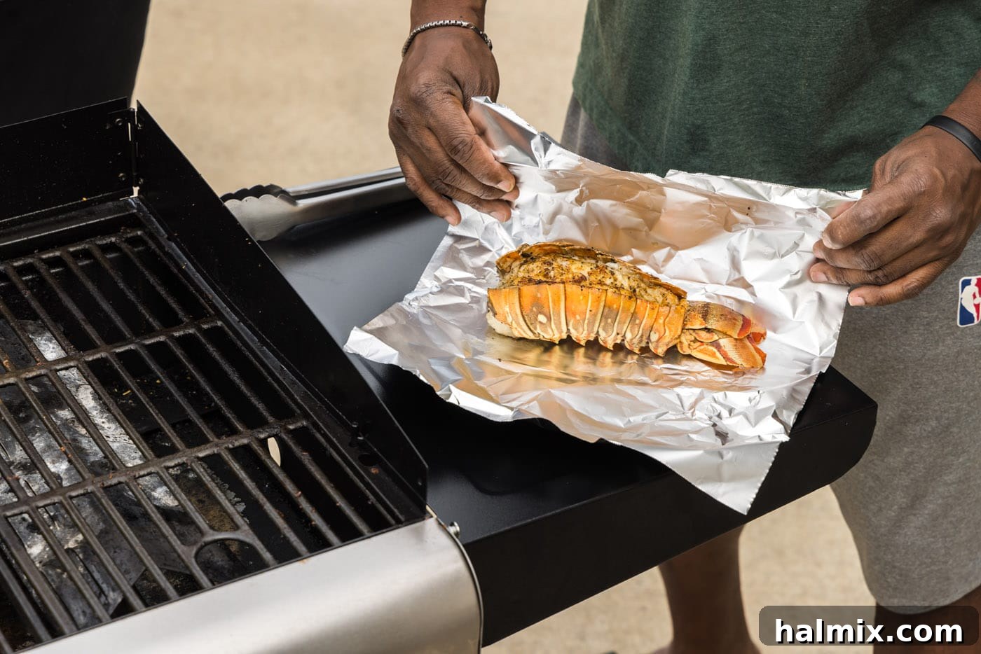 Wrapping freshly grilled lobster tail in aluminum foil to rest.