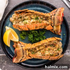 Overhead photo of two Grilled Lobster Tails on a plate with lemons, parsley, and melted butter for dipping.