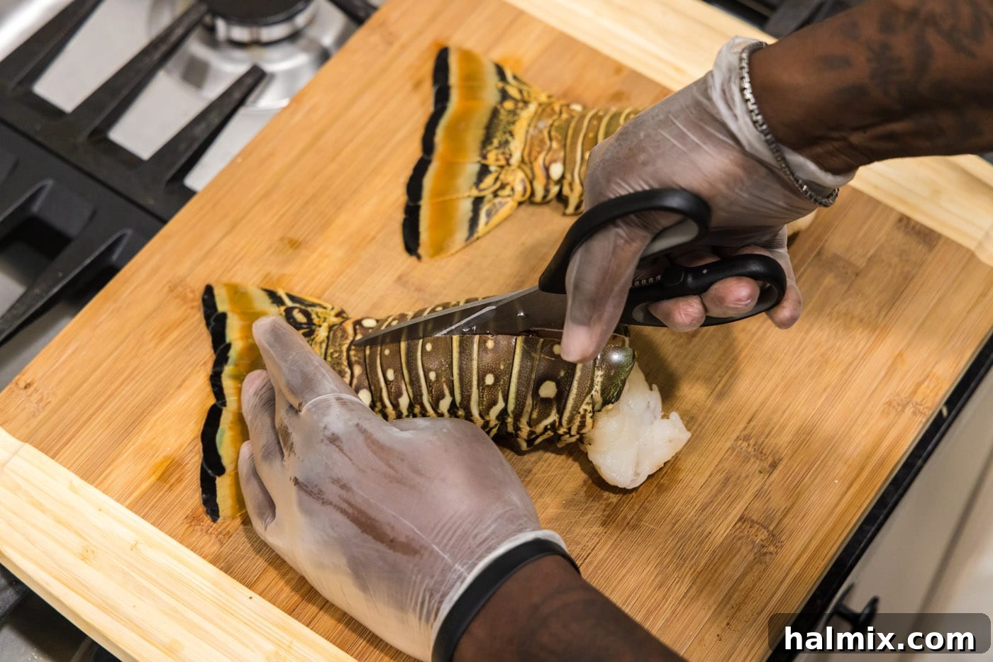 Using kitchen shears to meticulously cut down the center of a lobster tail shell, preparing it for grilling.