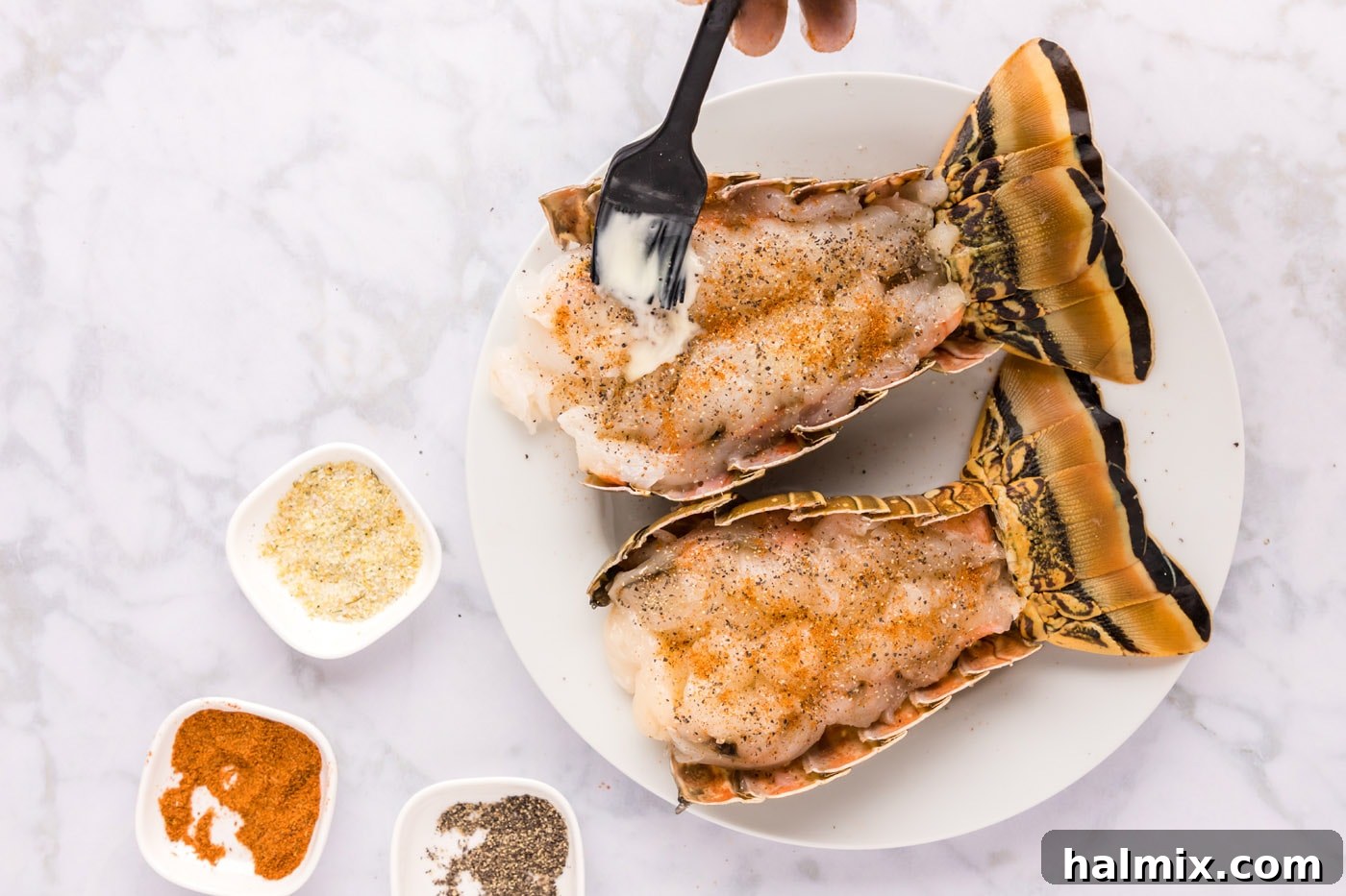 A pastry brush applying melted butter onto the seasoned lobster tail meat.