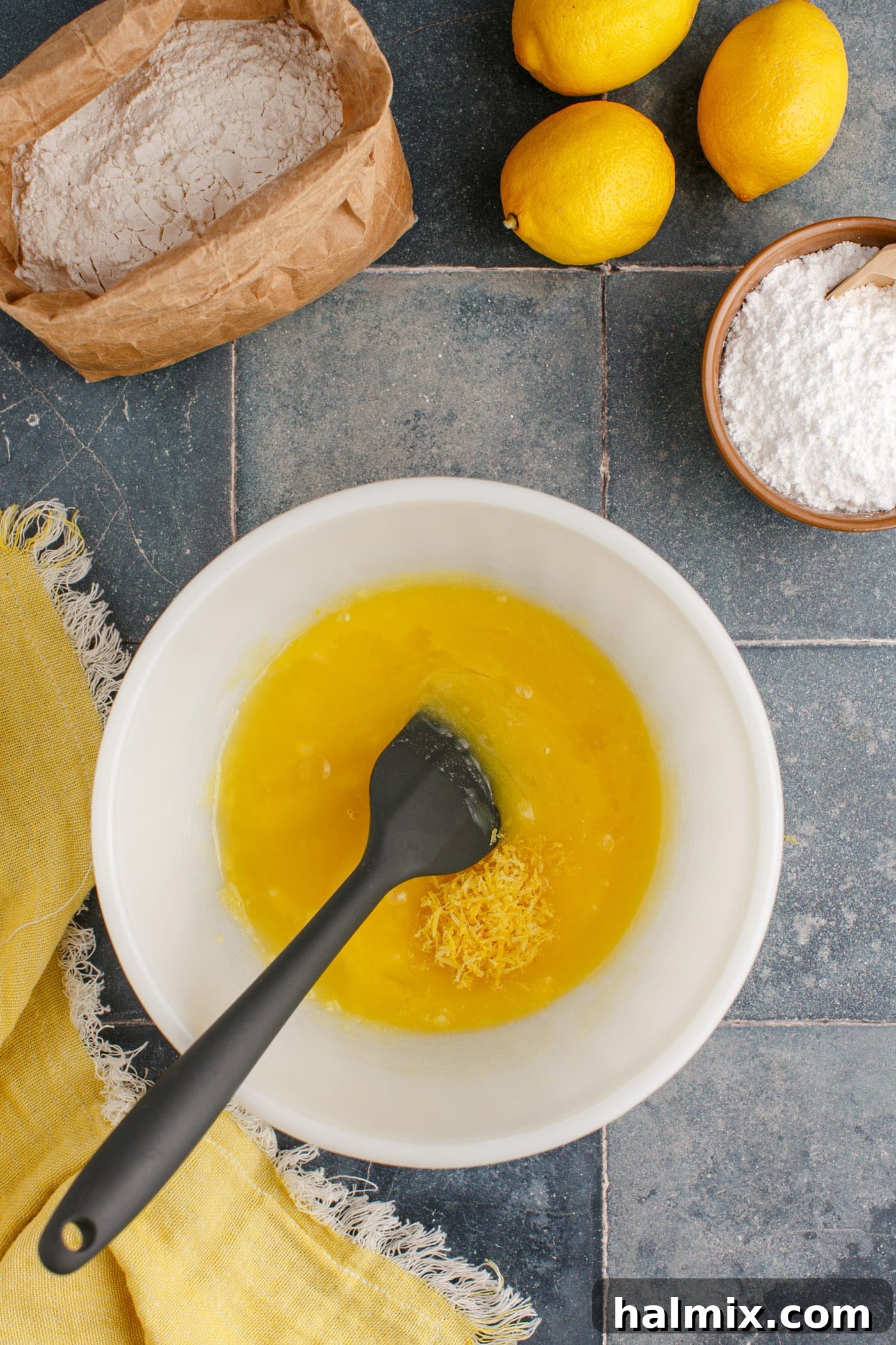Lemon juice and zest being added to the butter mixture in a bowl, stirred with a spatula.