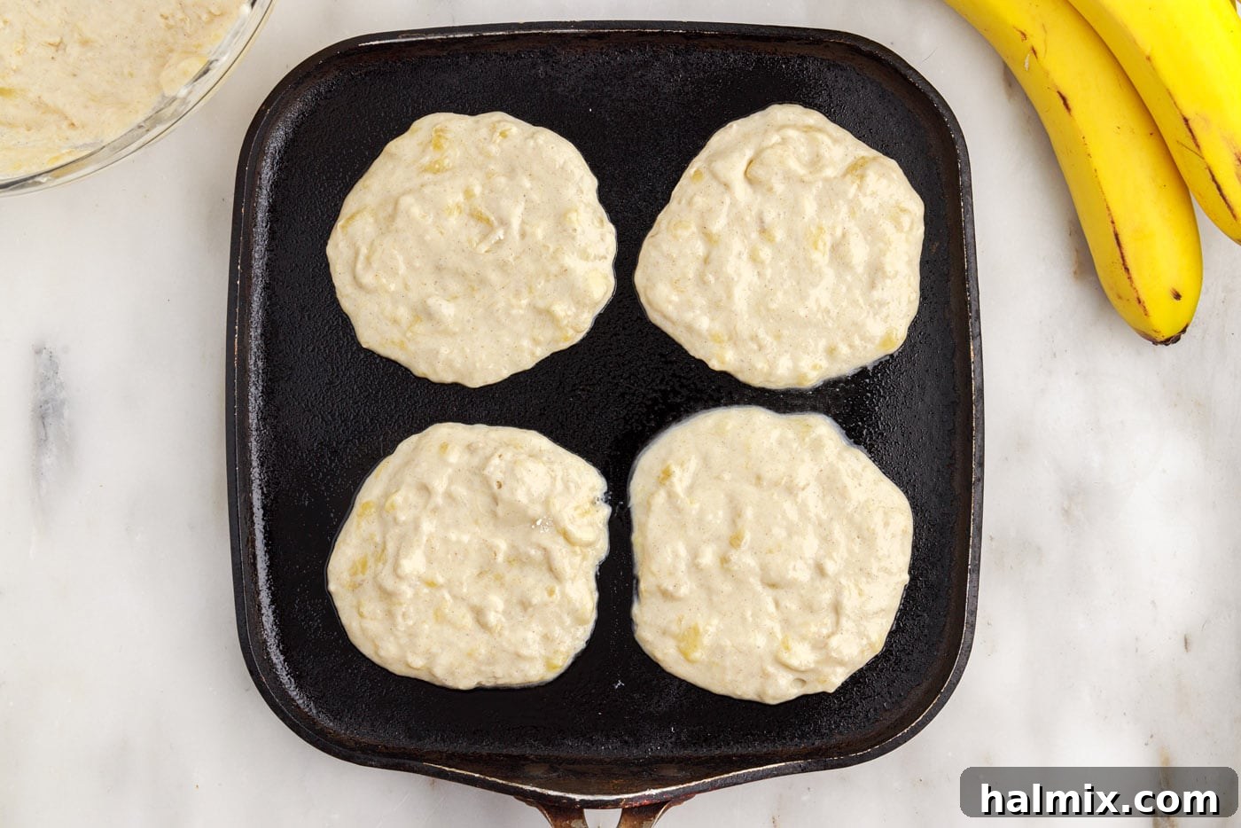 Banana pancake batter poured onto a hot griddle, beginning to cook