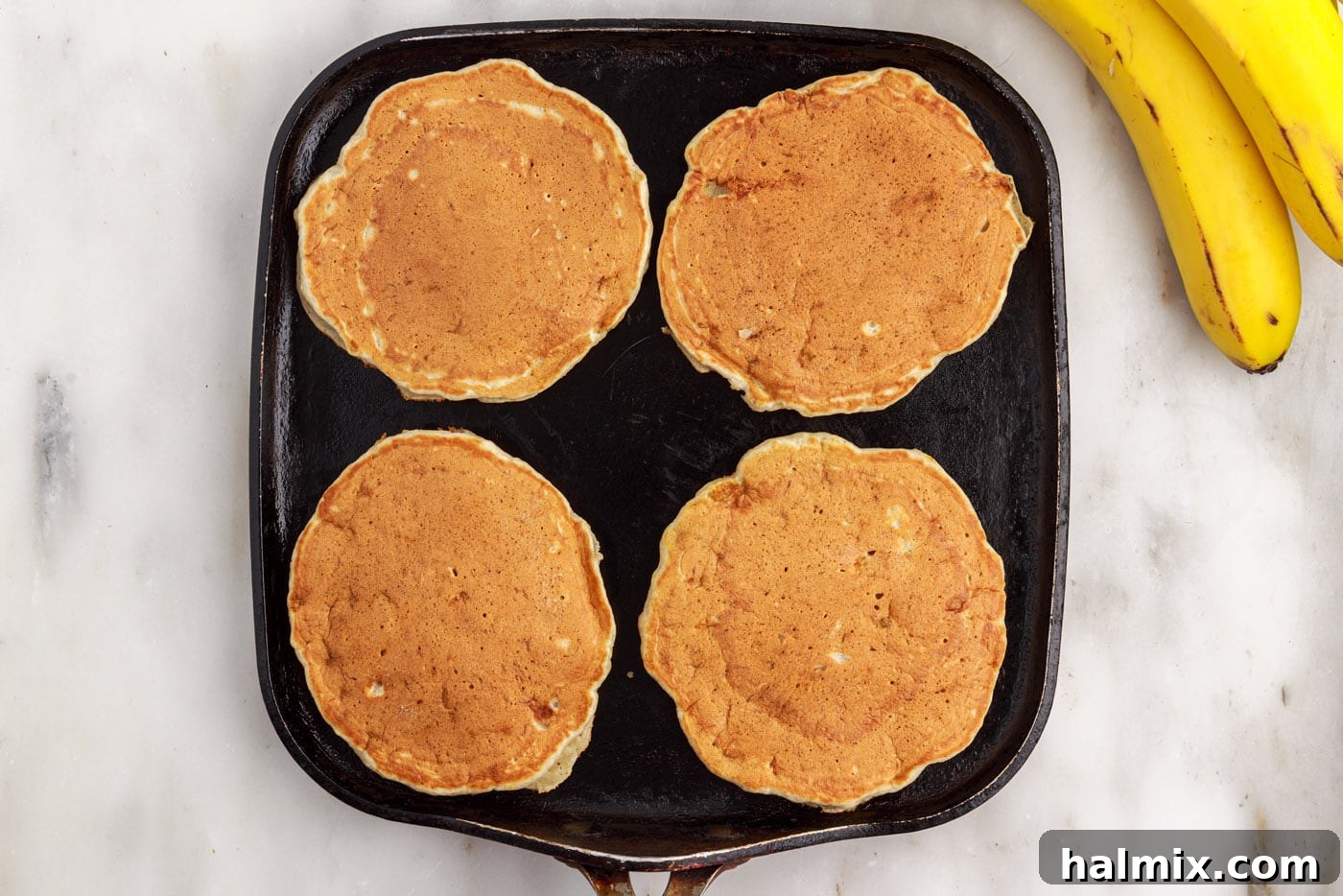 Golden brown banana pancakes cooking on a griddle, ready to be flipped to finish cooking