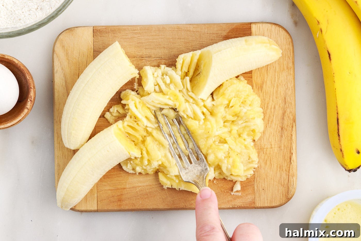 Mashing ripe bananas with a fork in a bowl, preparing them for the pancake batter
