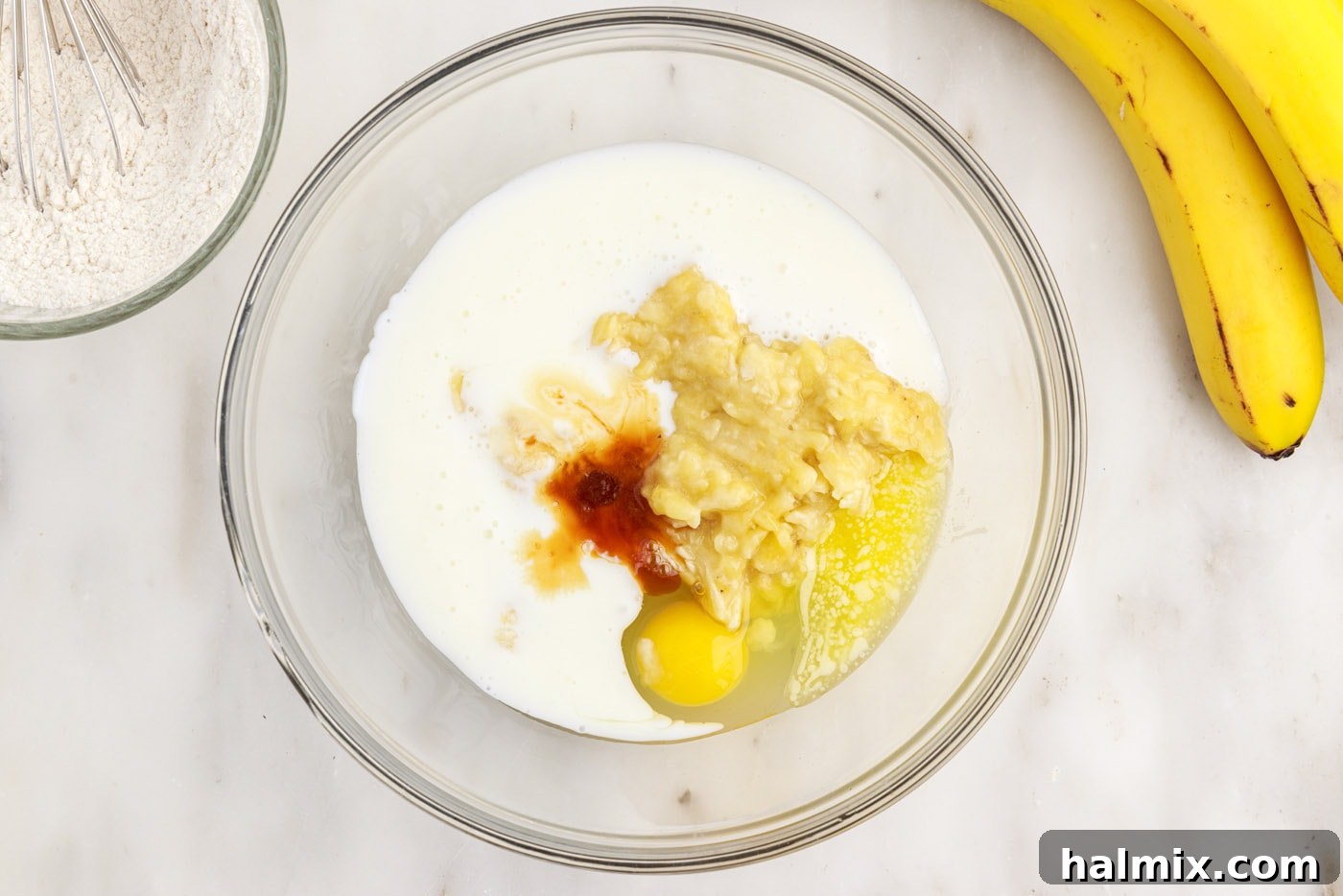 All the wet ingredients for banana pancake batter—egg, melted butter, vanilla, buttermilk, and mashed banana—in a mixing bowl