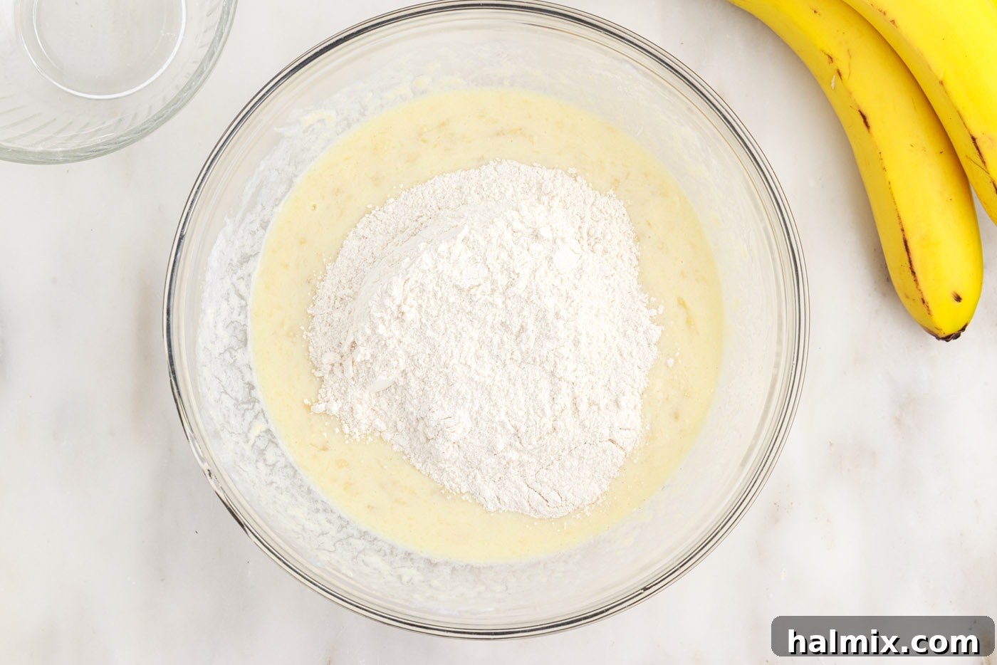 Adding dry ingredients to the wet banana pancake batter, preparing for gentle mixing