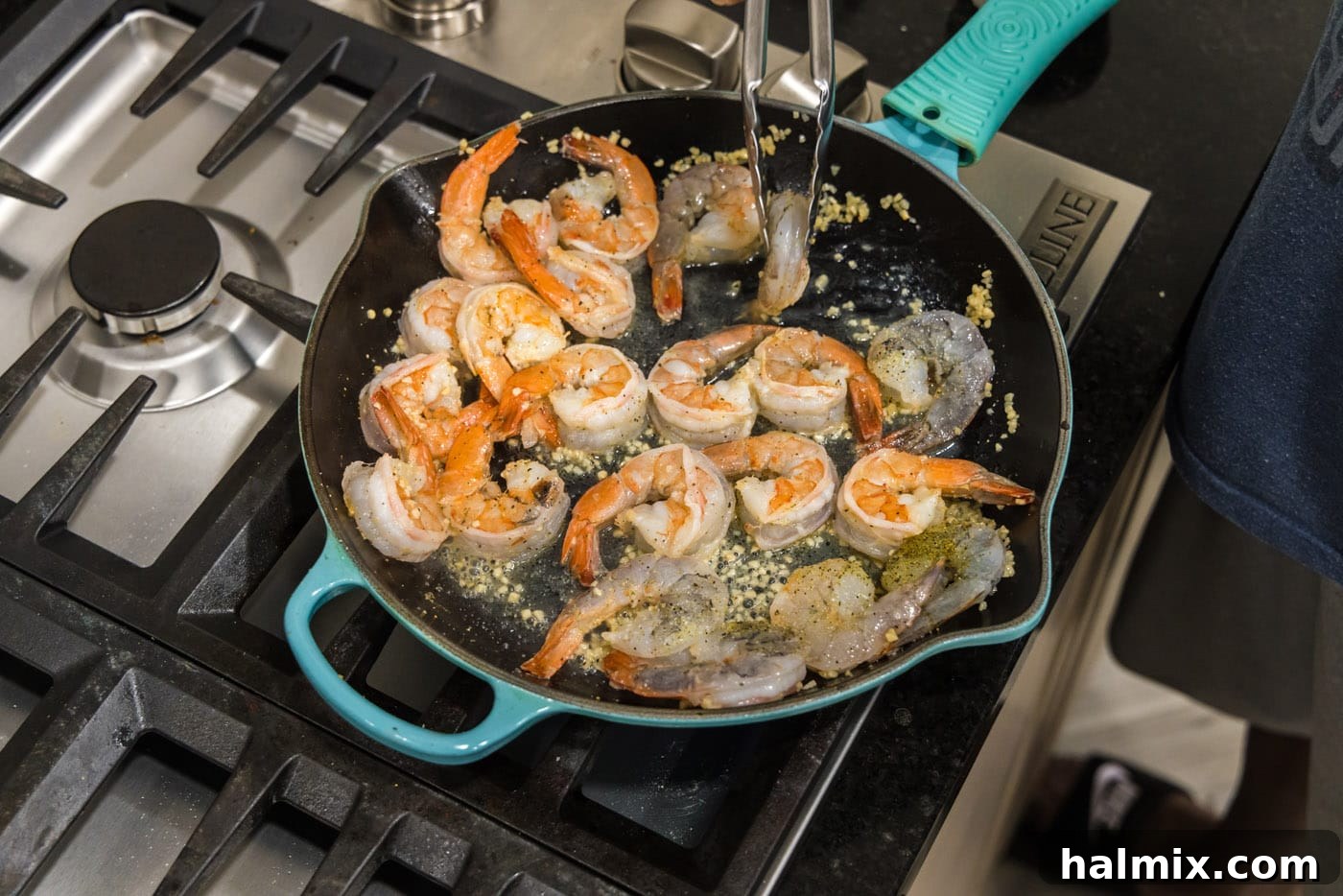 Tongs flipping shrimp over in a skillet to ensure even cooking