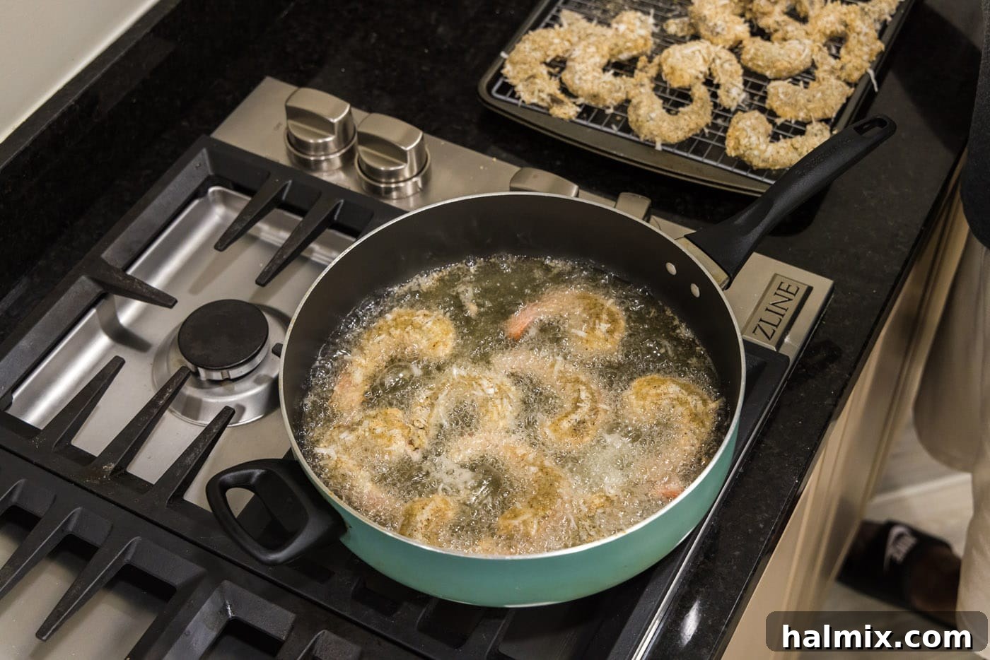 Coconut shrimp gently frying in hot oil in a deep skillet