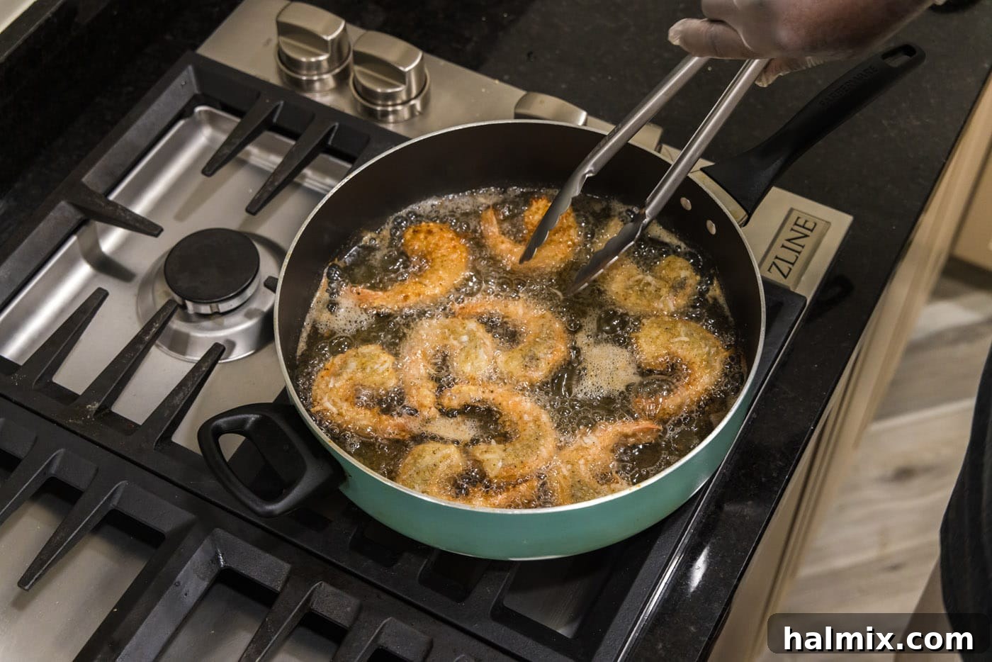 Crispy Coconut Shrimp 12 Tongs flipping coconut shrimp in the skillet to cook the other side