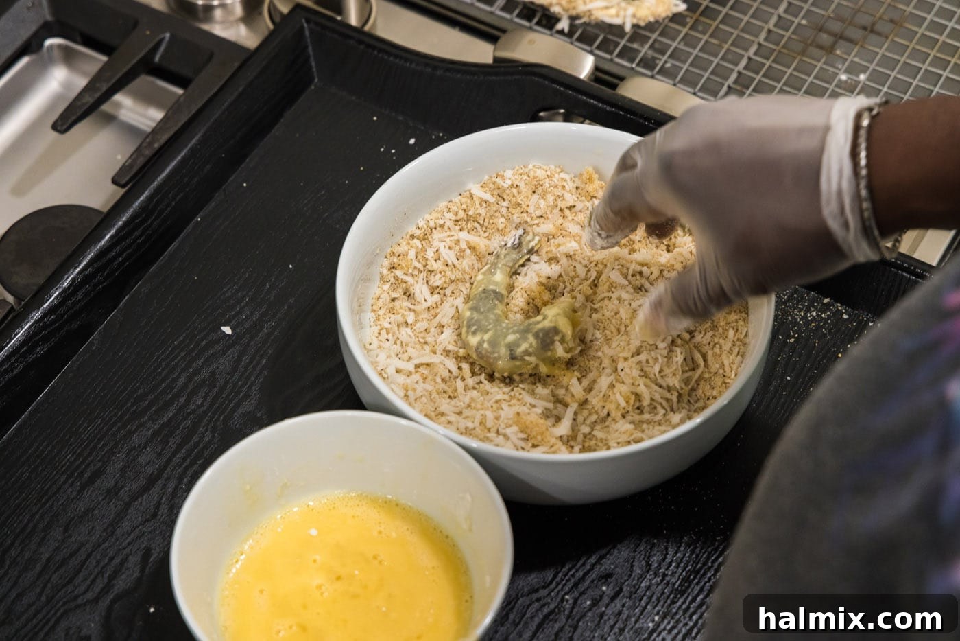 Crispy Coconut Shrimp 8 A hand pressing a dredged shrimp into the coconut and Panko breadcrumb mixture