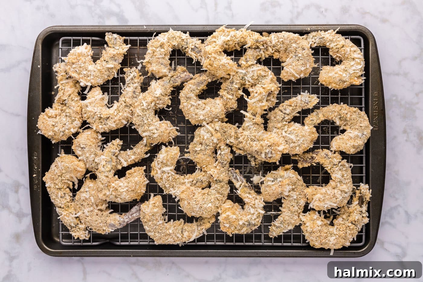 Neatly arranged coconut panko coated shrimp on a baking sheet with a wire rack