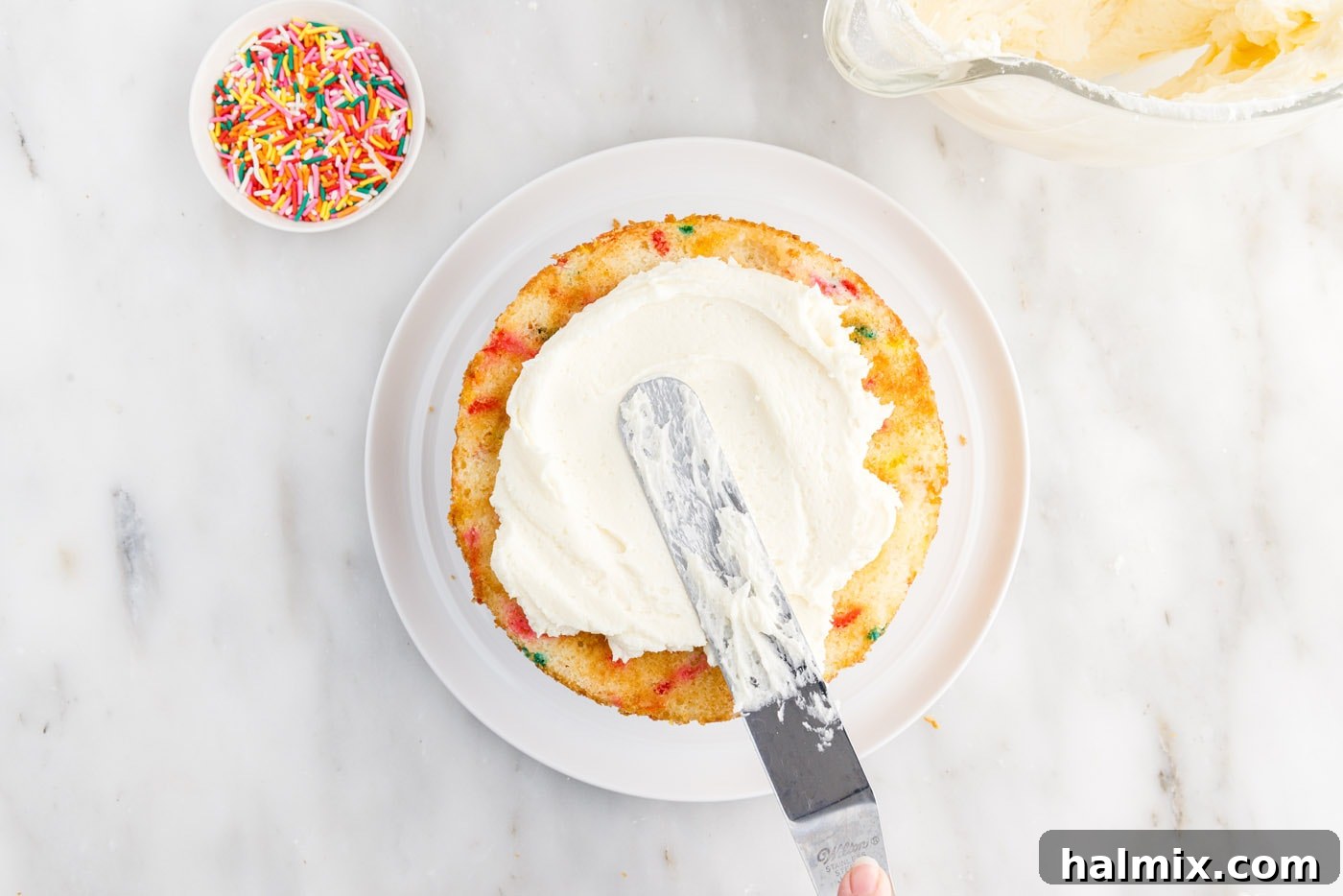 Festive Sprinkle Cake 20 spreading frosting over cake layer