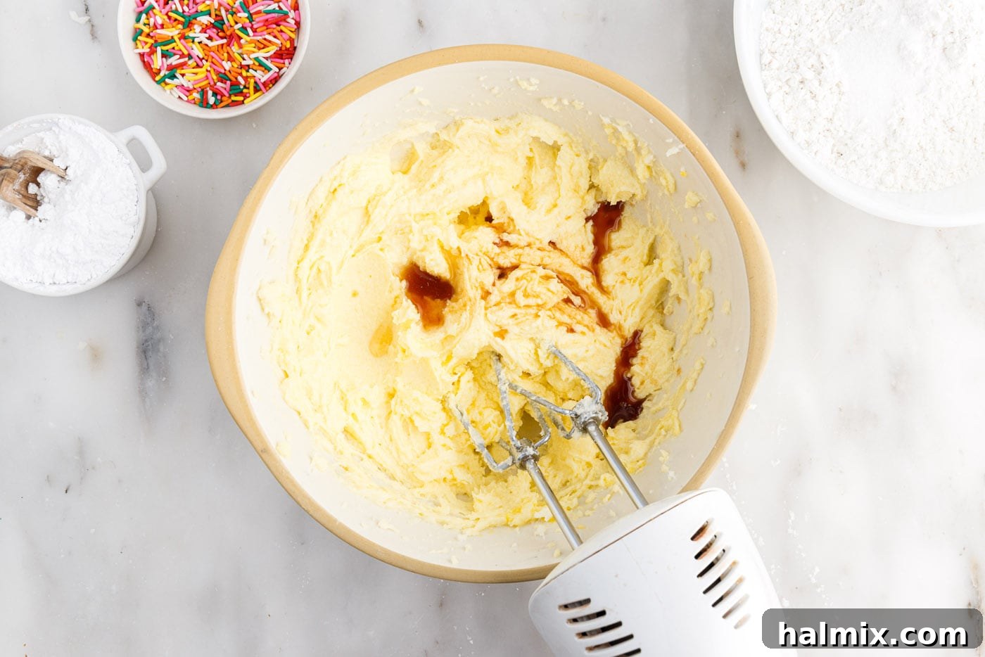 Festive Sprinkle Cake 7 beating vanilla, almond, and oil into butter and sugar mixture in a bowl